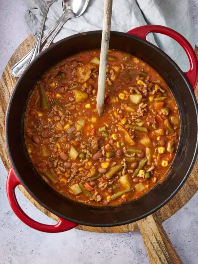 Overhead view of cowboy soup in a red pot with a wooden spoon.