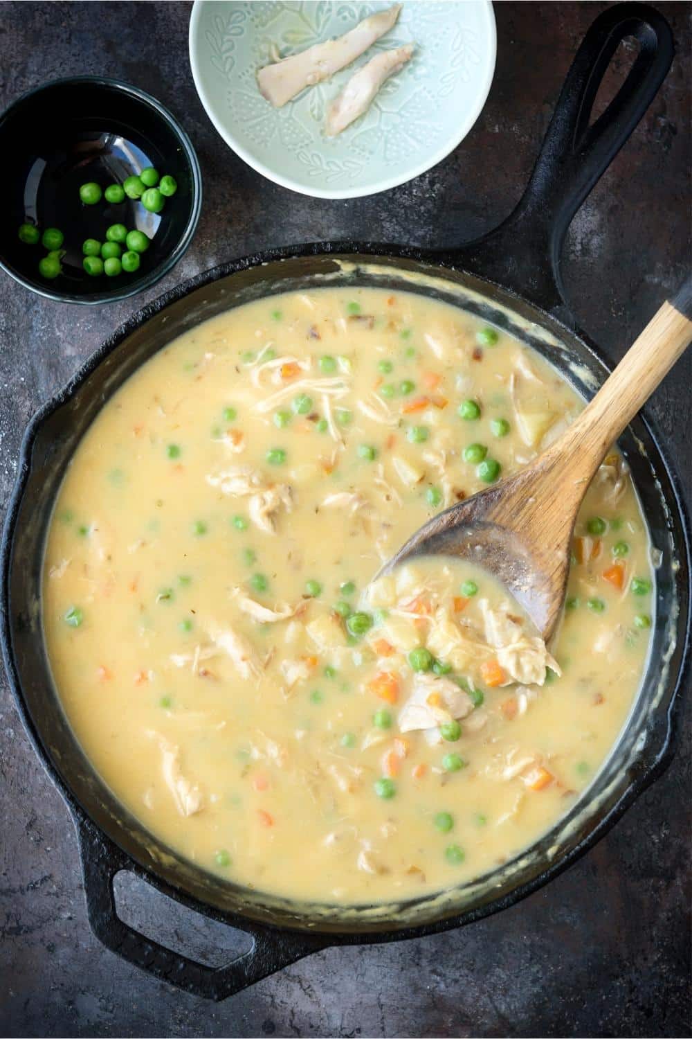 A cast iron pot of crustless chicken pot pie and a wooden spatula.