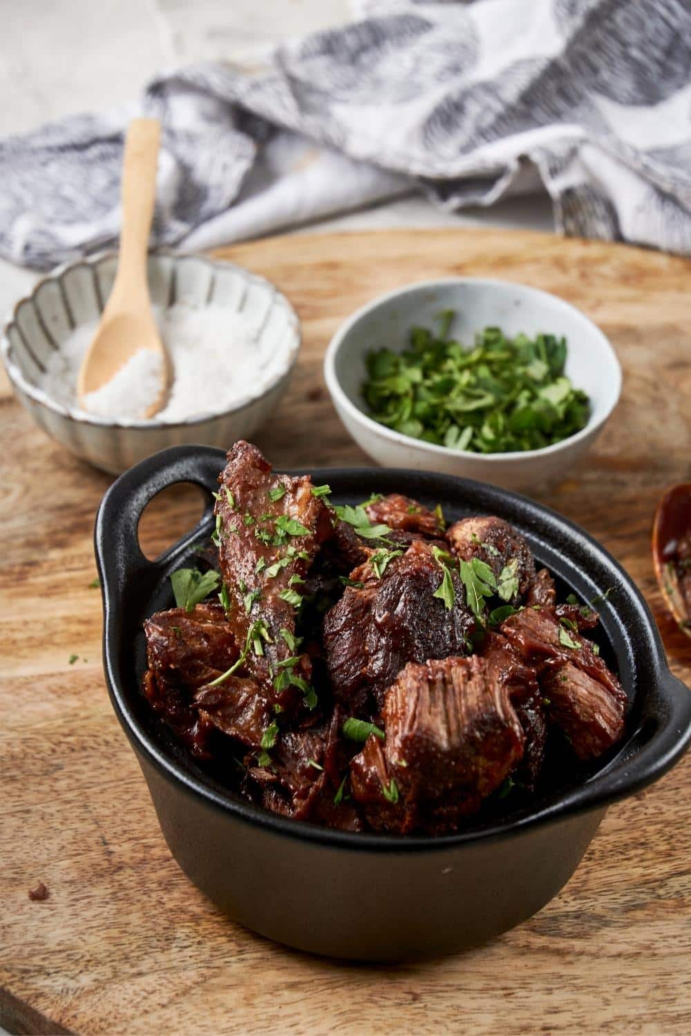 Burnt ends topped with fresh parsley in a small cast iron bowl, next to bowls of salt and parsley.