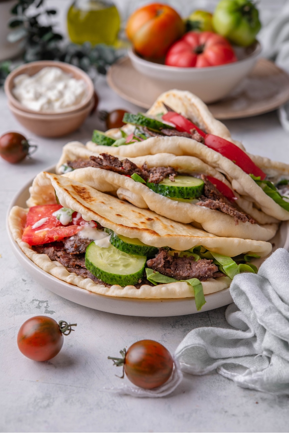 A gyro with tomato, cucumber, and sliced beef with two gyros behind them.