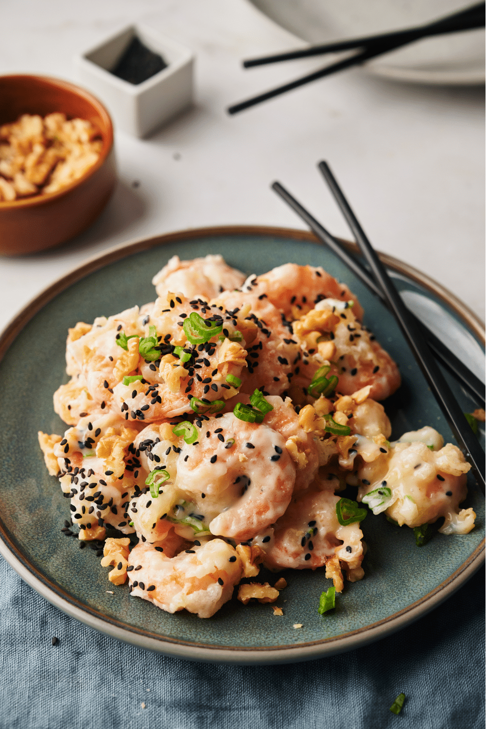 A plate of honey walnut shrimp garnished with sesame seeds, sliced green onions, and walnuts. A set of chopsticks is on the plate.