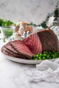 Sliced medium rare sirloin tip roast and green peas on a plate.