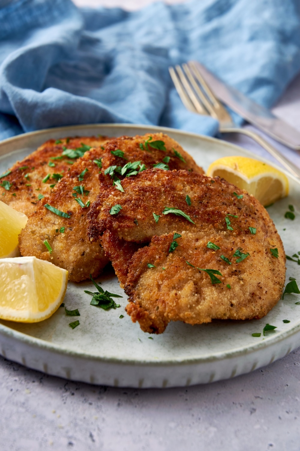 A closer look at crispy turkey cutlets on a plate garnished with fresh herbs and lemon wedges.