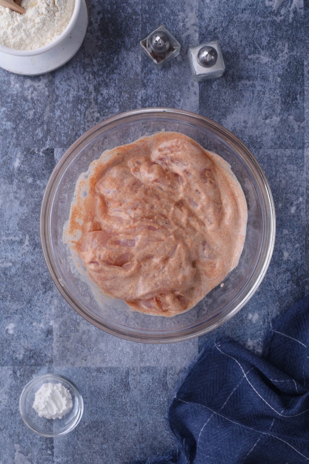 Raw chicken in a glass bowl filled with a marinade.