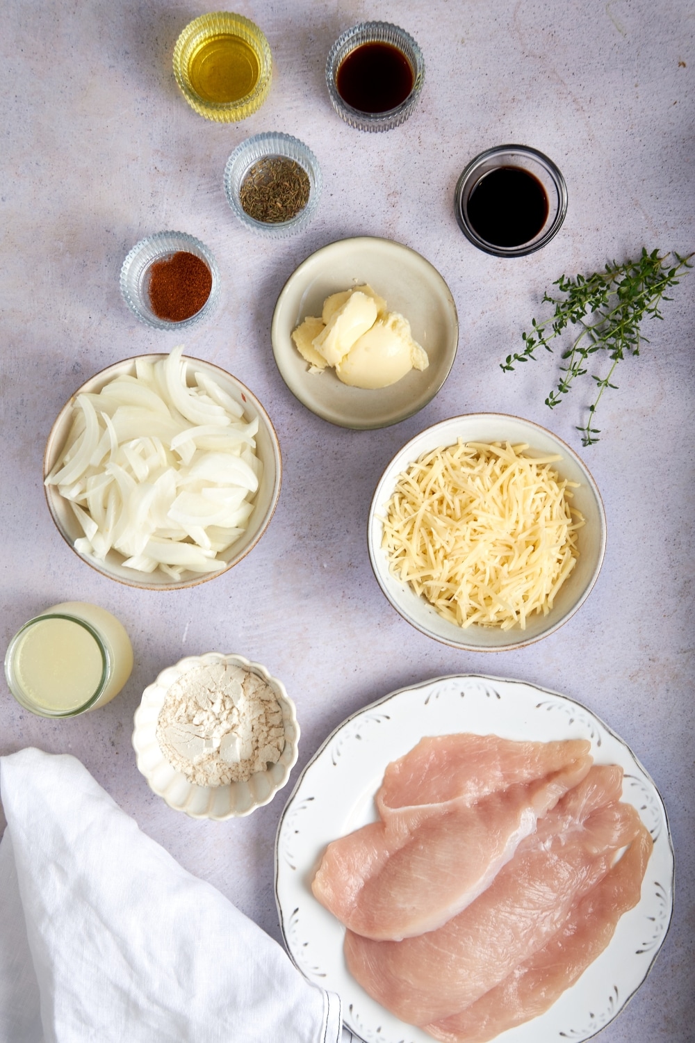 Bowls of chicken cutlets, flour, chicken broth, sliced onions, butter, grated Gruyere cheese, paprika, dried thyme, olive oil, balsamic vinegar, and Worcestershire sauce.