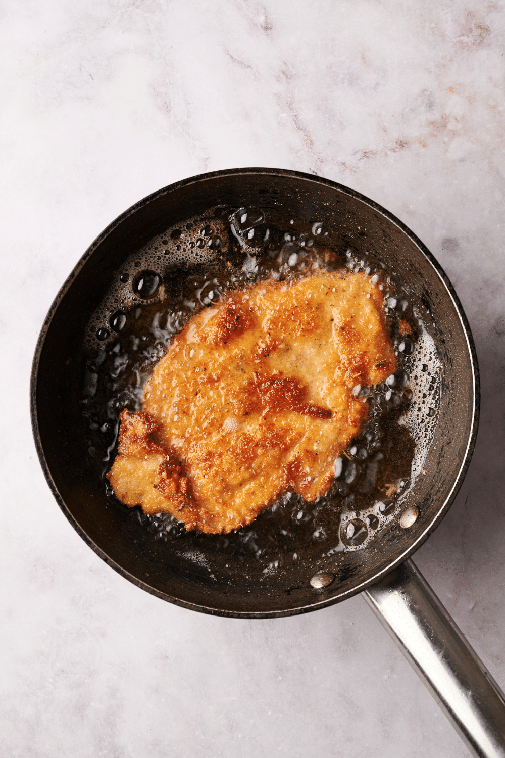 A pot with a breaded chicken cutlet frying in oil.