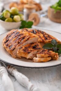 Sliced grilled chicken breasts garnished with fresh herbs on a white plate.