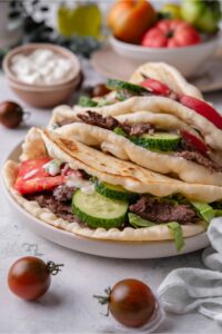 Two gyros on top of each other, each with thinly sliced meat, sliced cucumber, lettuce, tomato and tzatziki sauce.
