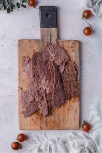 A wooden board filled with thinly sliced beef.