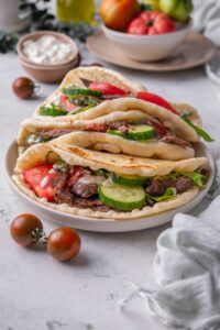 Three gyros piled on top of each other, each with thinly sliced meat, sliced cucumber, lettuce, tomato and tzatziki sauce.
