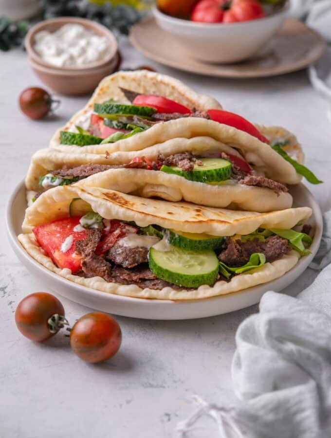 Three gyros piled on top of each other, each with thinly sliced meat, sliced cucumber, lettuce, tomato and tzatziki sauce.