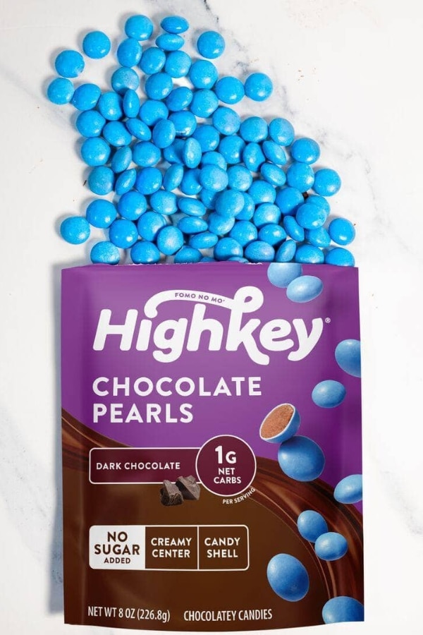 A bunch of blue chocolate pearls coming out of a bag of Highkey chocolate pearls.