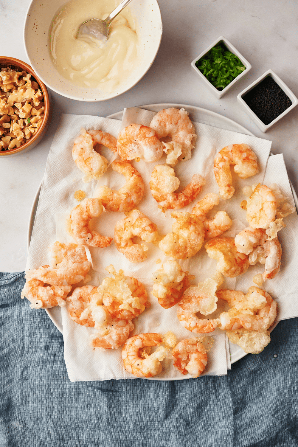 Fried shrimp on a paper towel lined plate. The shrimp is surrounded by an assortment of ingredients.