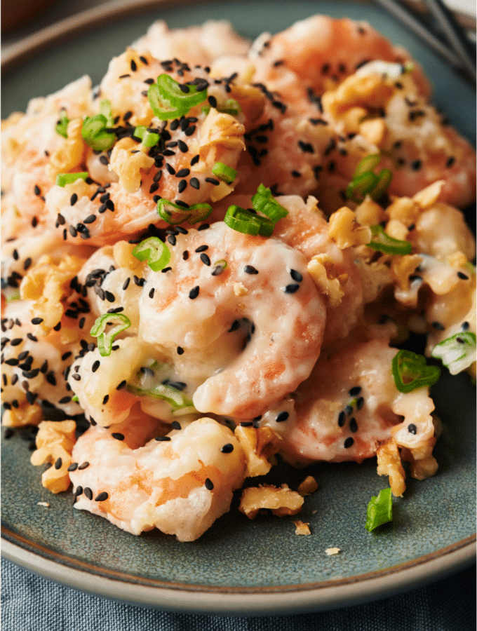 A plate of honey walnut shrimp garnished with sesame seeds, sliced green onions, and walnuts.