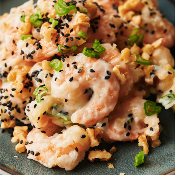 A plate of honey walnut shrimp garnished with sesame seeds, sliced green onions, and walnuts.