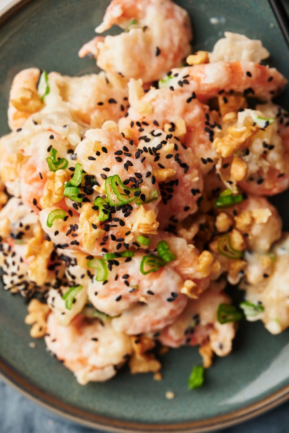 Sesame seeds, chopped walnuts, and green onions on top of a bunch of shrimp on a plate.