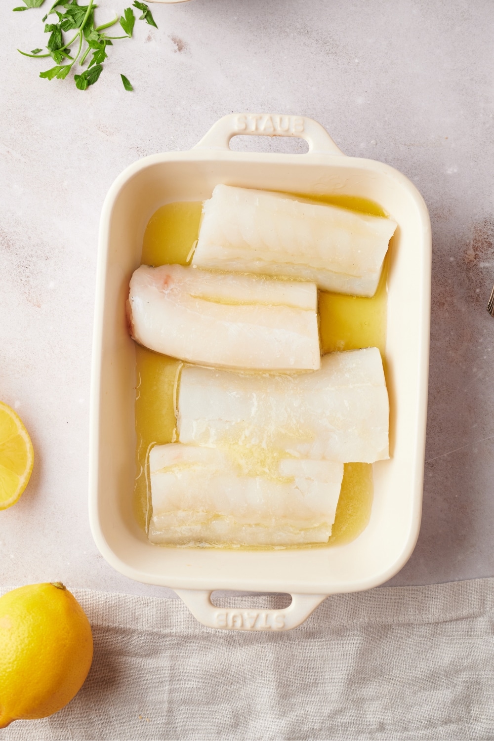 Four mahi mahi fillets on top of oil in a white baking dish.