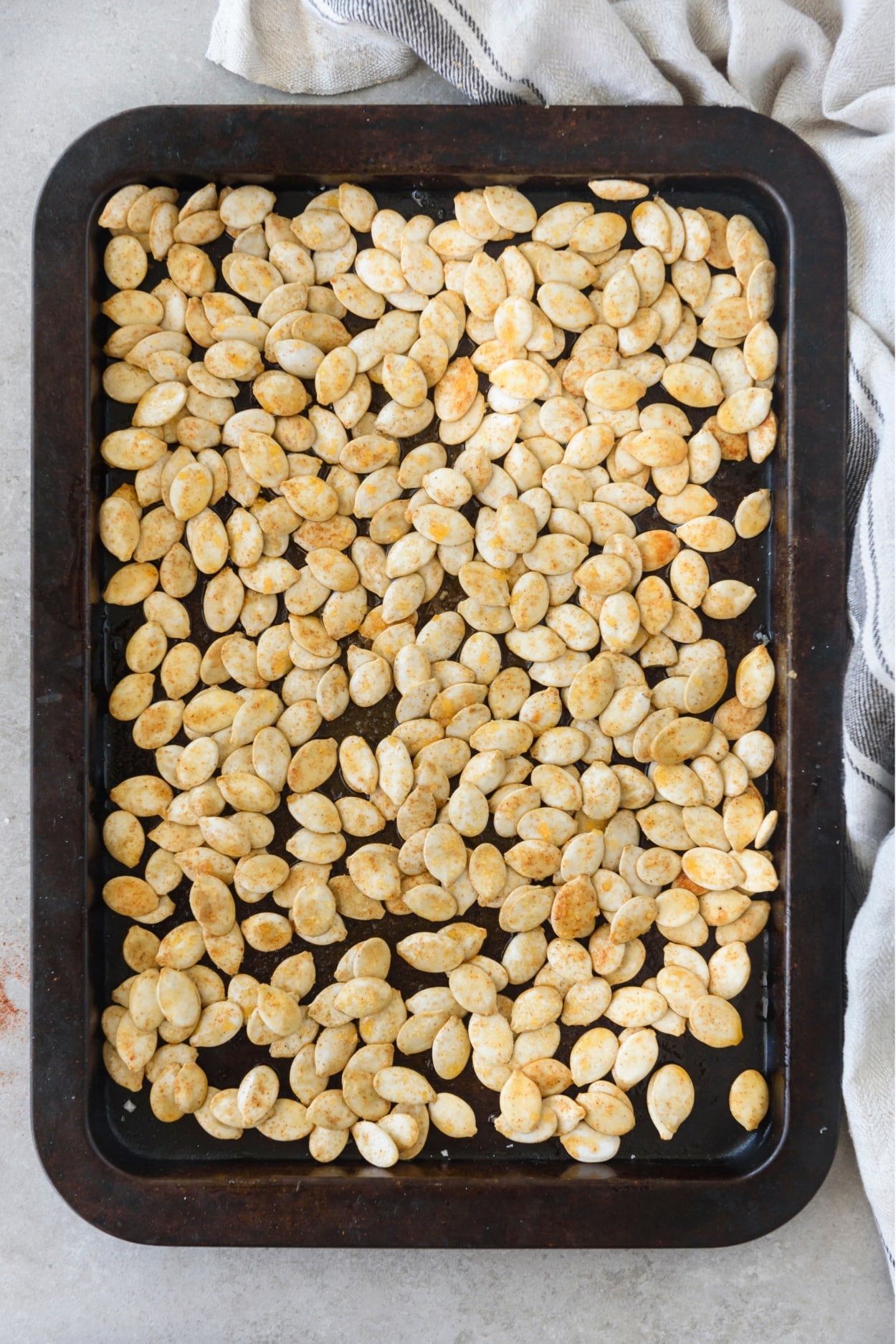 Seasoned pumpkin seeds spread out on a baking sheet.