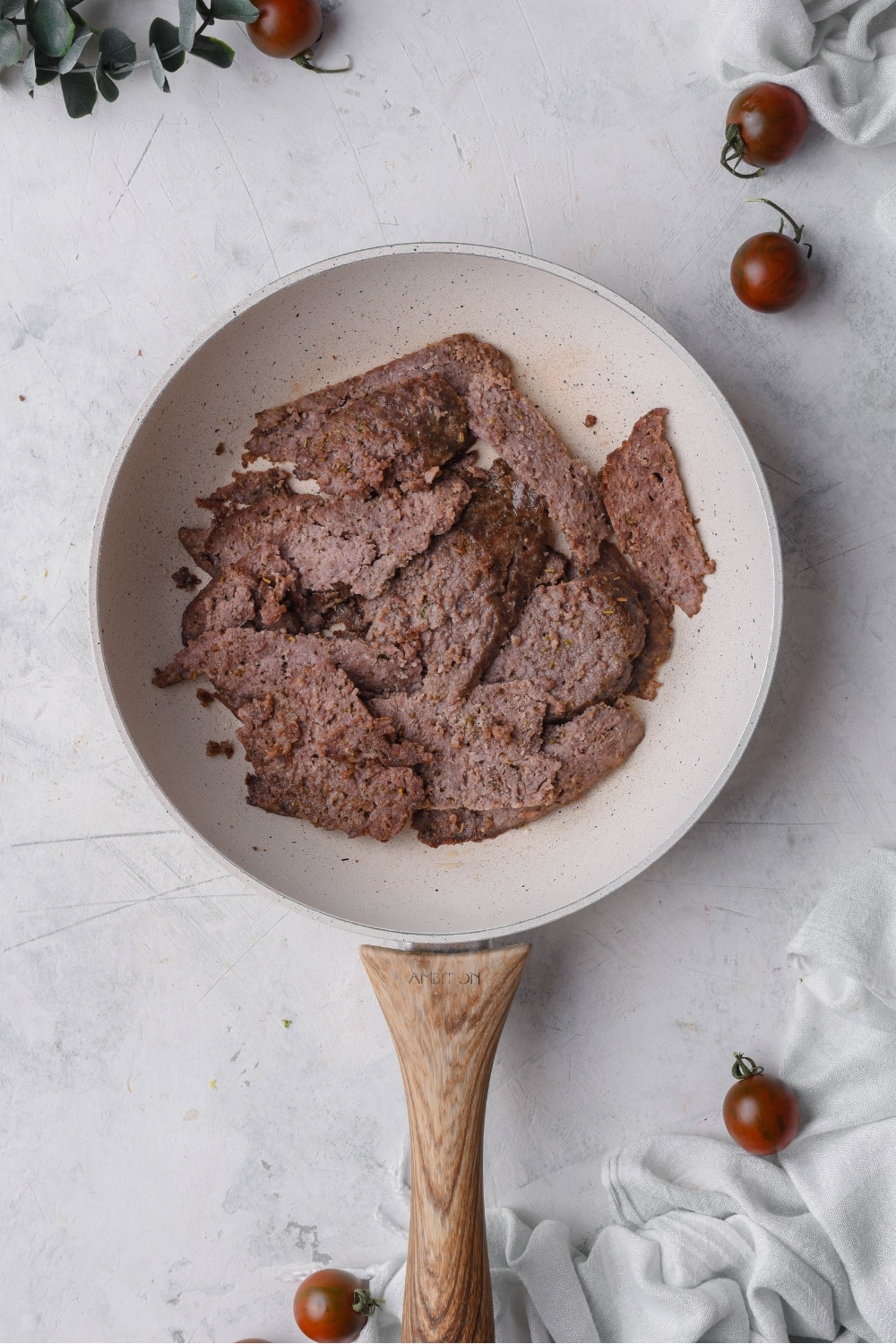 A skillet with thinly sliced meat cooking in it.