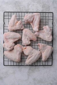 Raw chicken wings coated in flour on top of a wire rack on a counter.
