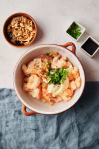 A bowl of fried shrimp with a creamy sauce on top. The shrimp is garnished with walnuts, green onions, and sesame seeds.