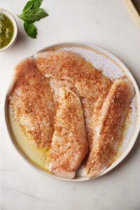 Four pieces of seasoned catfish on a white plate.