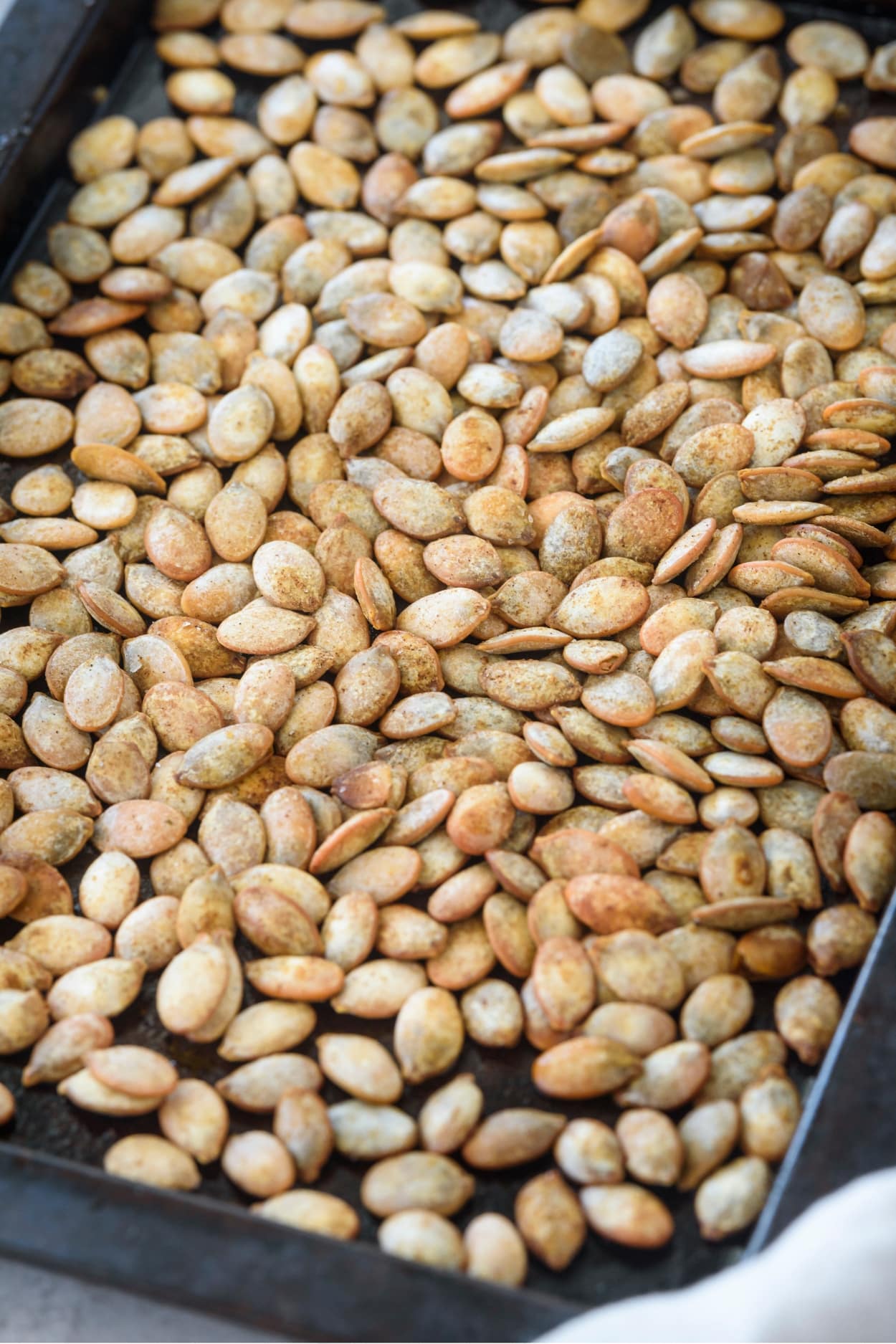 Part of a baking sheet that is filled with pumpkin seeds.