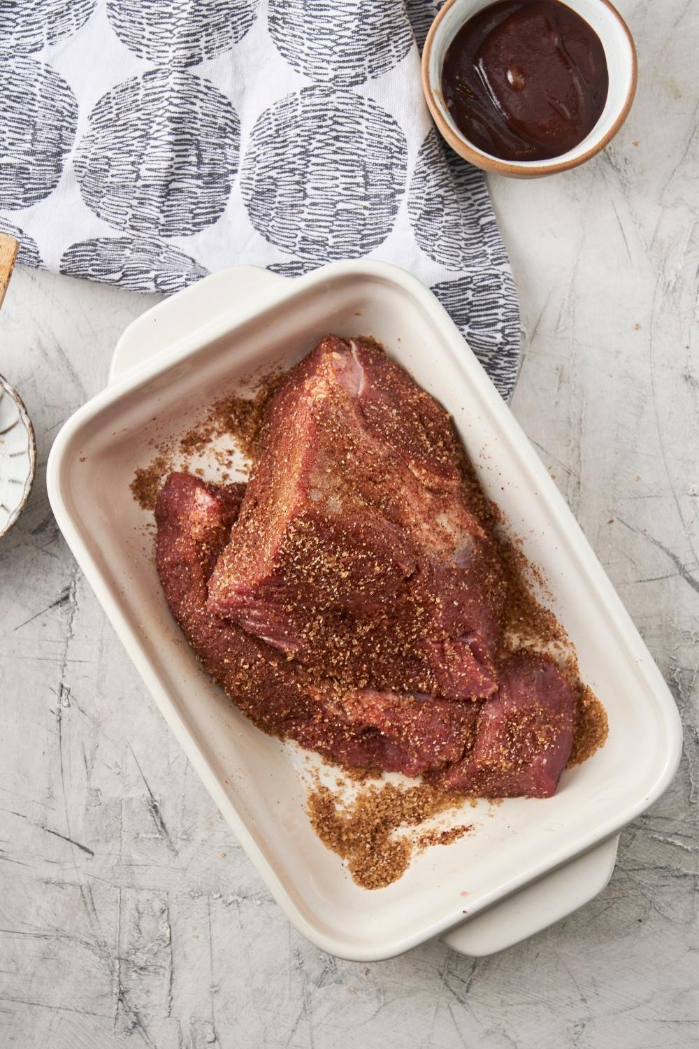 Chuck roast covered in dry rub in a casserole dish.