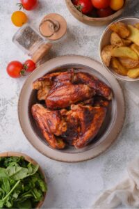 A bunch of bbq chicken wings in a bowl on top of a plate on a counter.