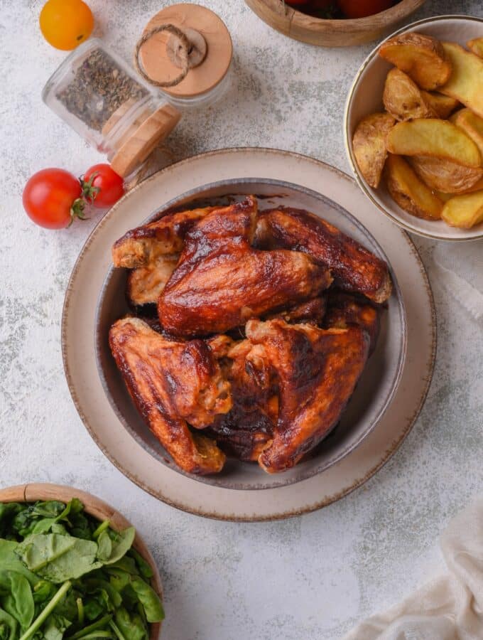 A bunch of bbq chicken wings in a bowl on top of a plate on a counter.