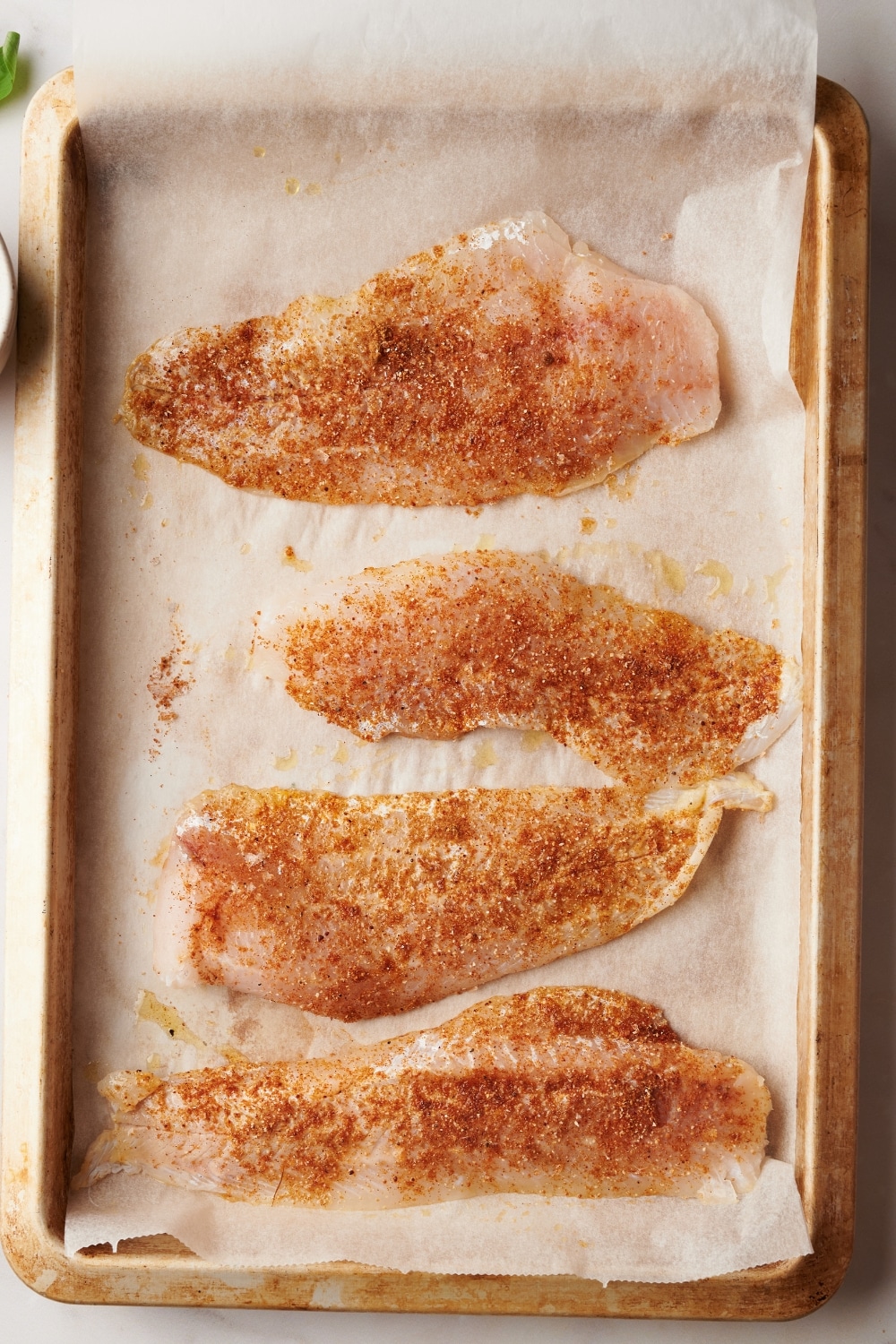 Four pieces of seasoned catfish on top of a piece of parchment paper on a baking sheet.