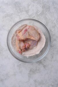 A bowl of chicken wings in a flour mixture.
