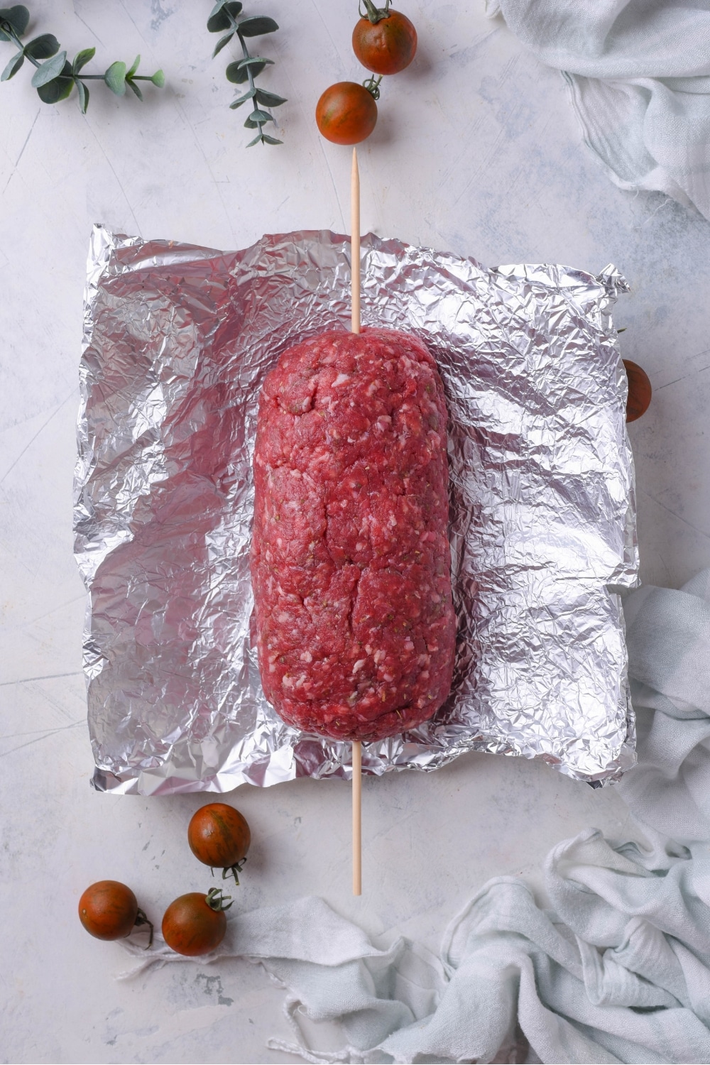 A log of raw ground beef atop foil with a skewer down the center.