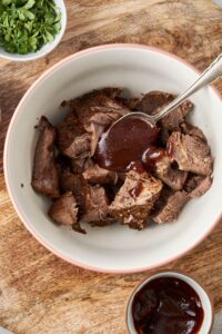 Chopped chuck roast pieces in a bowl with a spoon of bbq sauce.