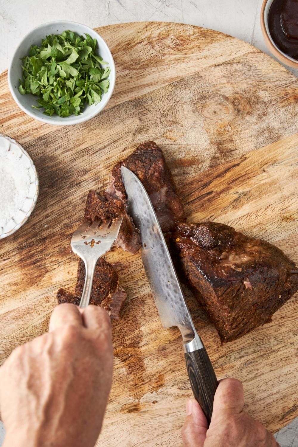 Slicing chuck roast into chunks with a knife and fork.