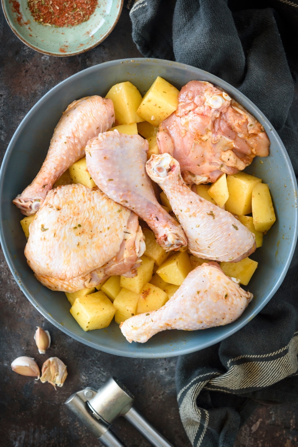 Raw chicken on top of potaotes in a black bowl.