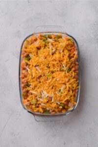 A baking dish filled with enchilada casserole covered in shredded cheese.