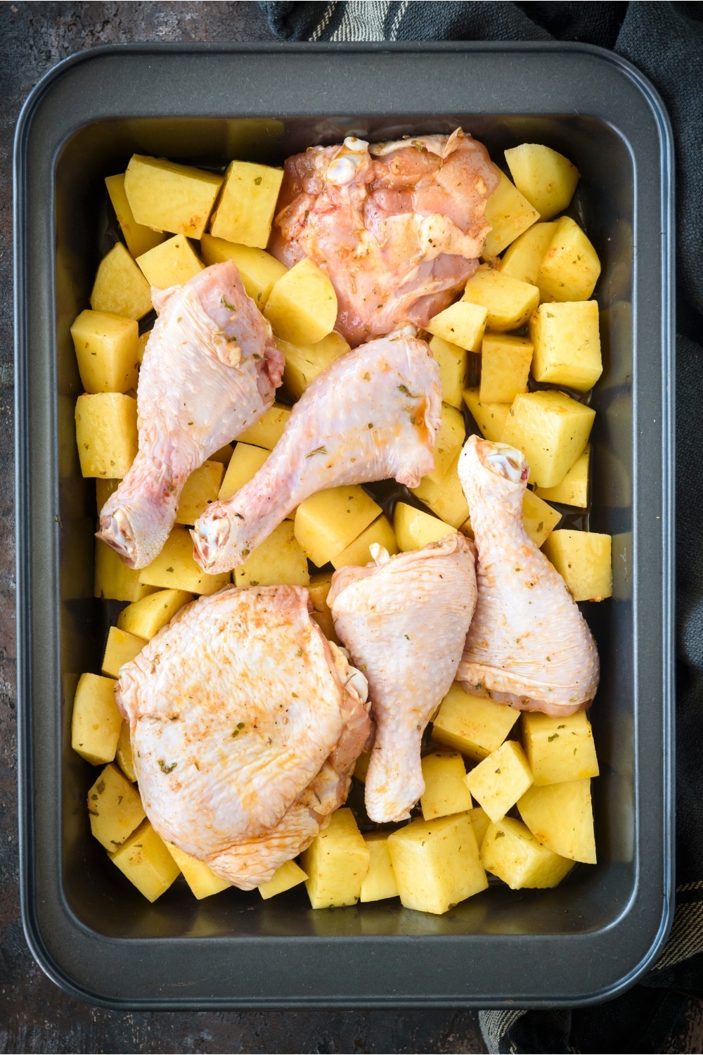 A bunch of chicken pieces on top of potatoes in a baking dish.