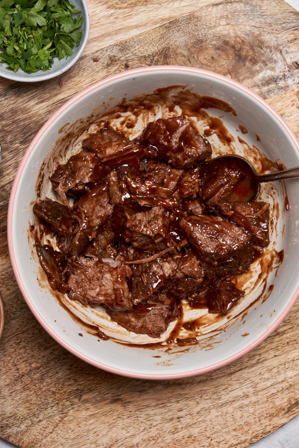 Chopped chuck roast pieces coated in bbq sauce in a bowl with a spoon.