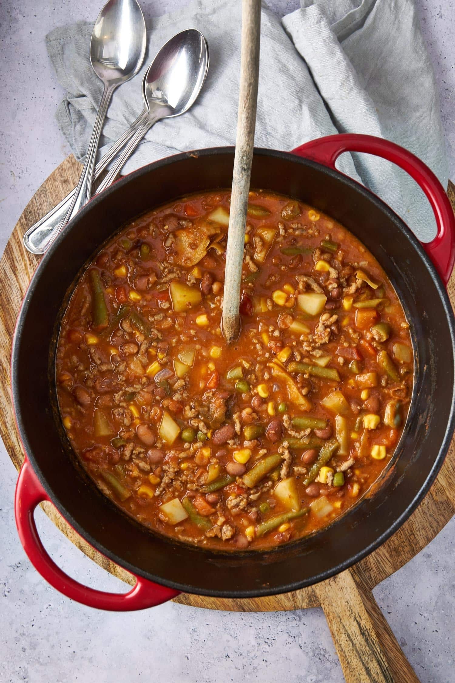 Overhead view of cowboy soup in a red pot with a wooden spoon.