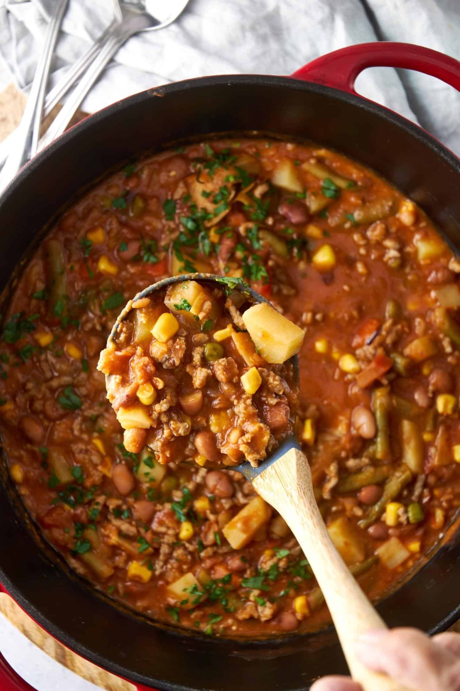 A portion of cowboy soup in a soup ladle, over a full pot.