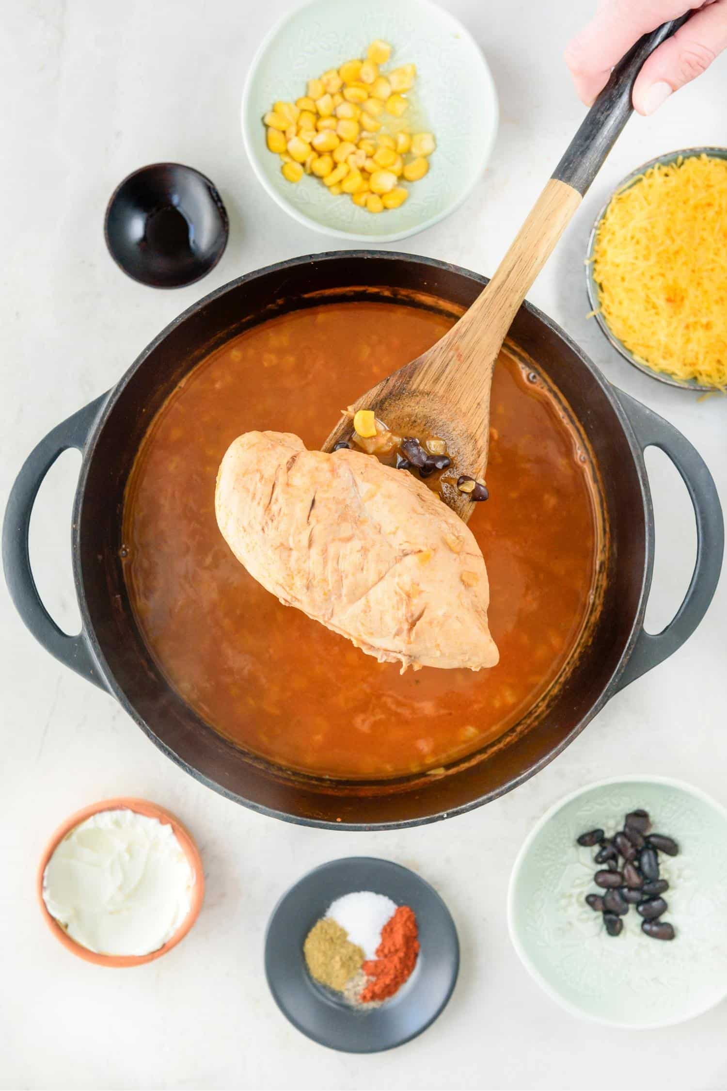 Cooked chicken breast on a wooden spatula over a pot of chicken enchilada soup.