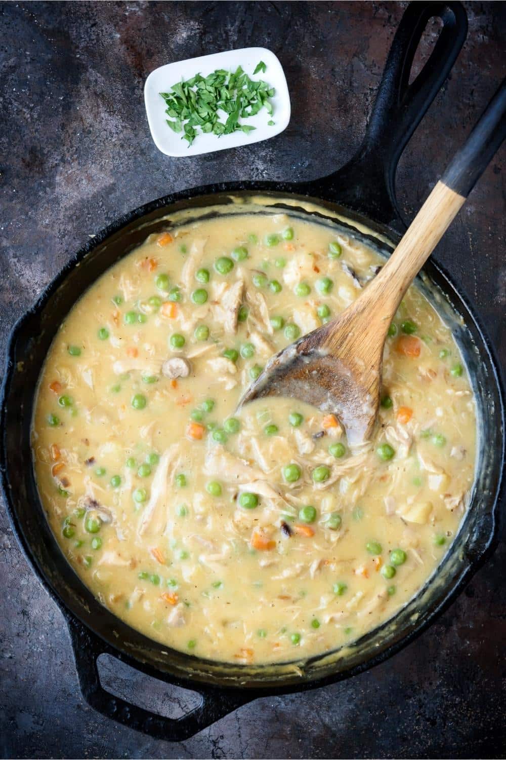 A wooden spatula in a large cast iron pot of crustless chicken pot pie.