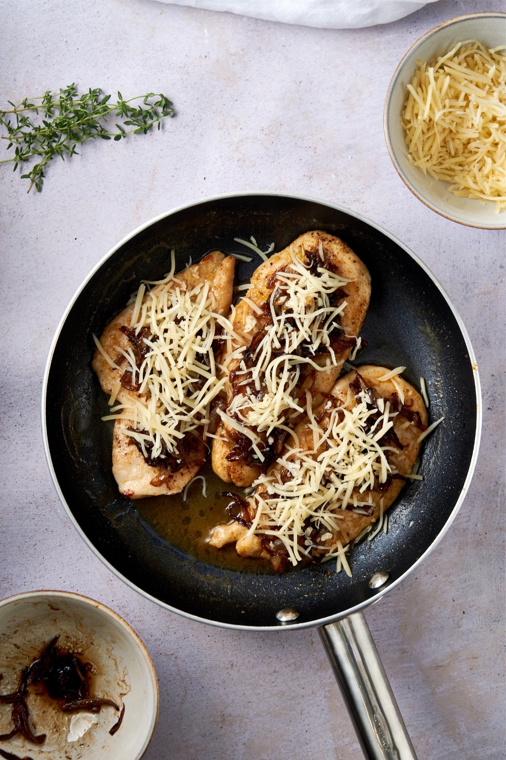 Chicken cutlets in a skillet topped with caramelized onions and shredded cheese.