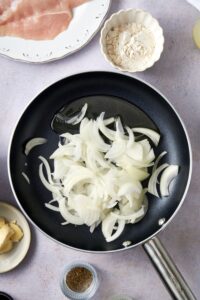 Sliced white onions in a skillet with olive oil.