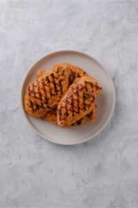 Overhead view of grilled chicken breasts piled on a white plate.