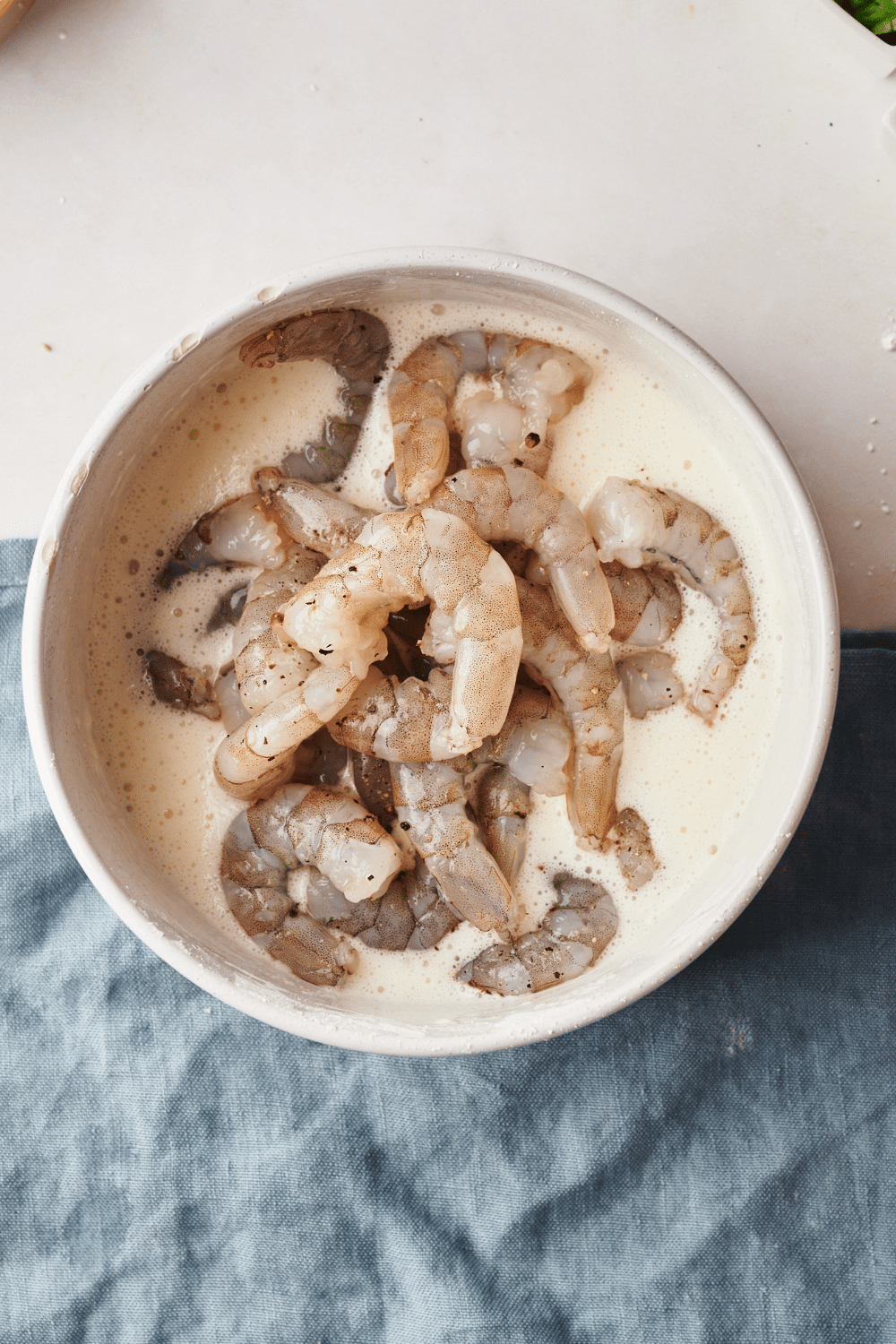 A white bowl filled with raw shrimp in a creamy sauce.