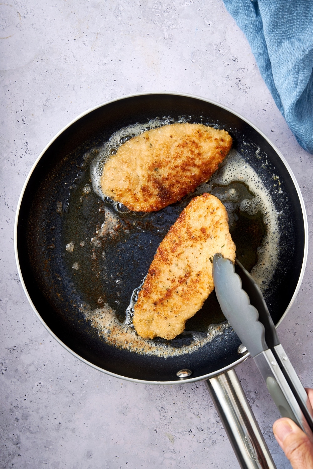 Taking cooked turkey cutlets out of the skillet with tongs.