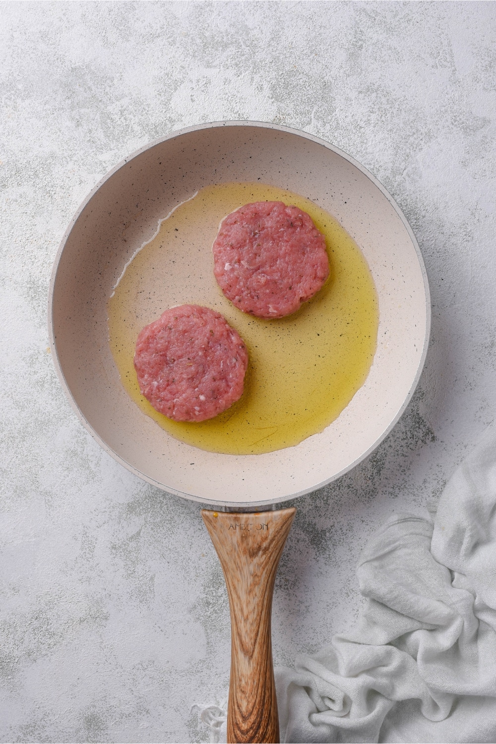 Two turkey sausage patties in a skillet with olive oil.