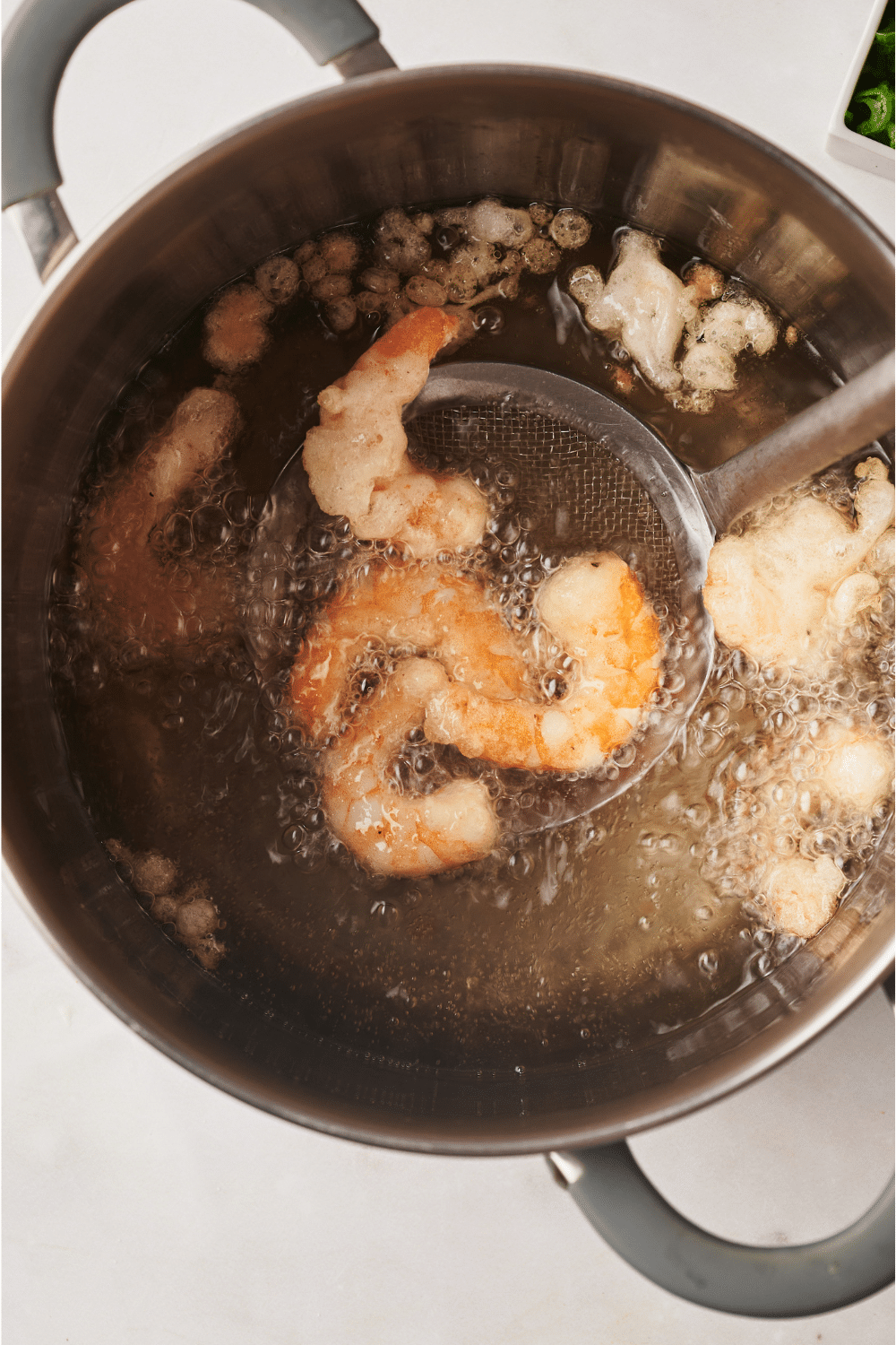 A pot of oil with shrimp frying in it and a strainer spoon removing the shrimp from the pot.